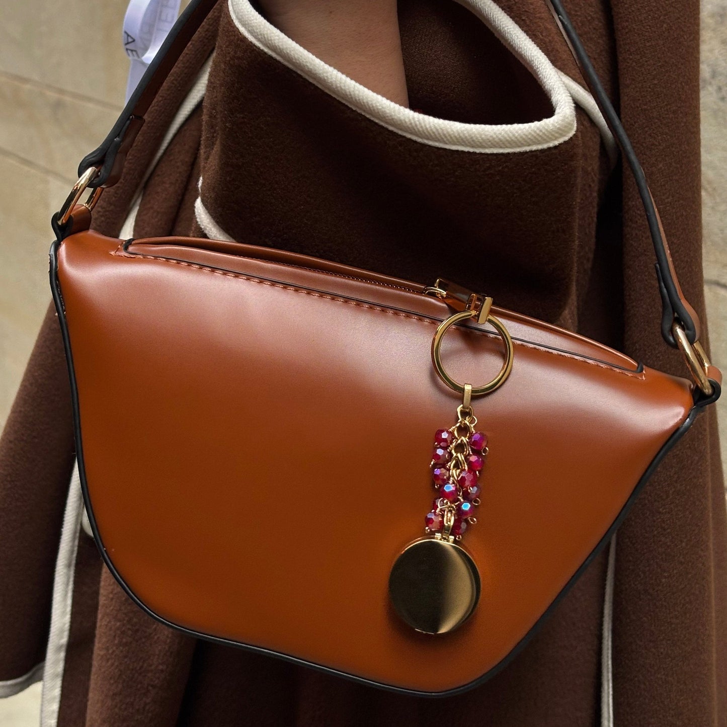 January Birthstone Pocket Locket Keychain hanging on the outside of a bag, featuring a vibrant red Garnet crystal and elegant gold stainless steel design. The keychain adds a stylish pop of colour and a personal touch to your accessories, perfect for showcasing your unique style.