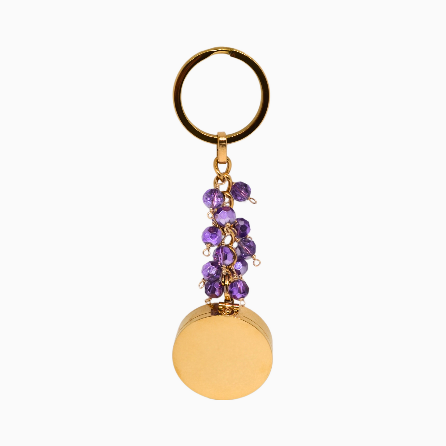 A gold stainless steel Amethyst Pocket Locket Keychain with a vibrant purple glass crystal, hanging elegantly. The locket is open to reveal a built-in mirror and a versatile compartment, perfect for storing small essentials. A thoughtful gift for February birthdays or anyone drawn to Amethyst’s calming energy.