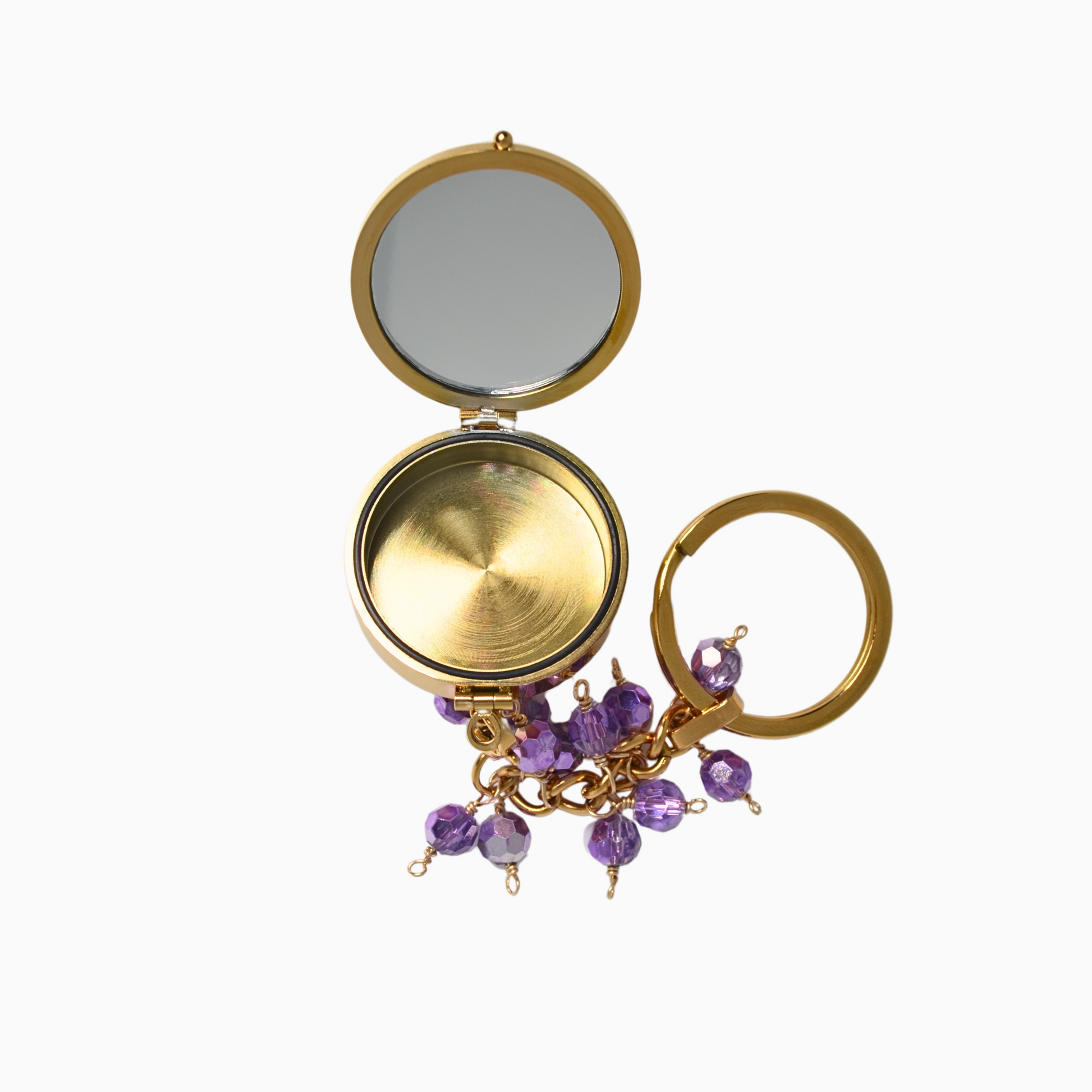 The Amethyst Pocket Locket Keychain opened to reveal its built-in mirror and hidden compartment. The gold stainless steel locket shines alongside its vibrant purple glass crystal, making it both stylish and functional for carrying small essentials.
