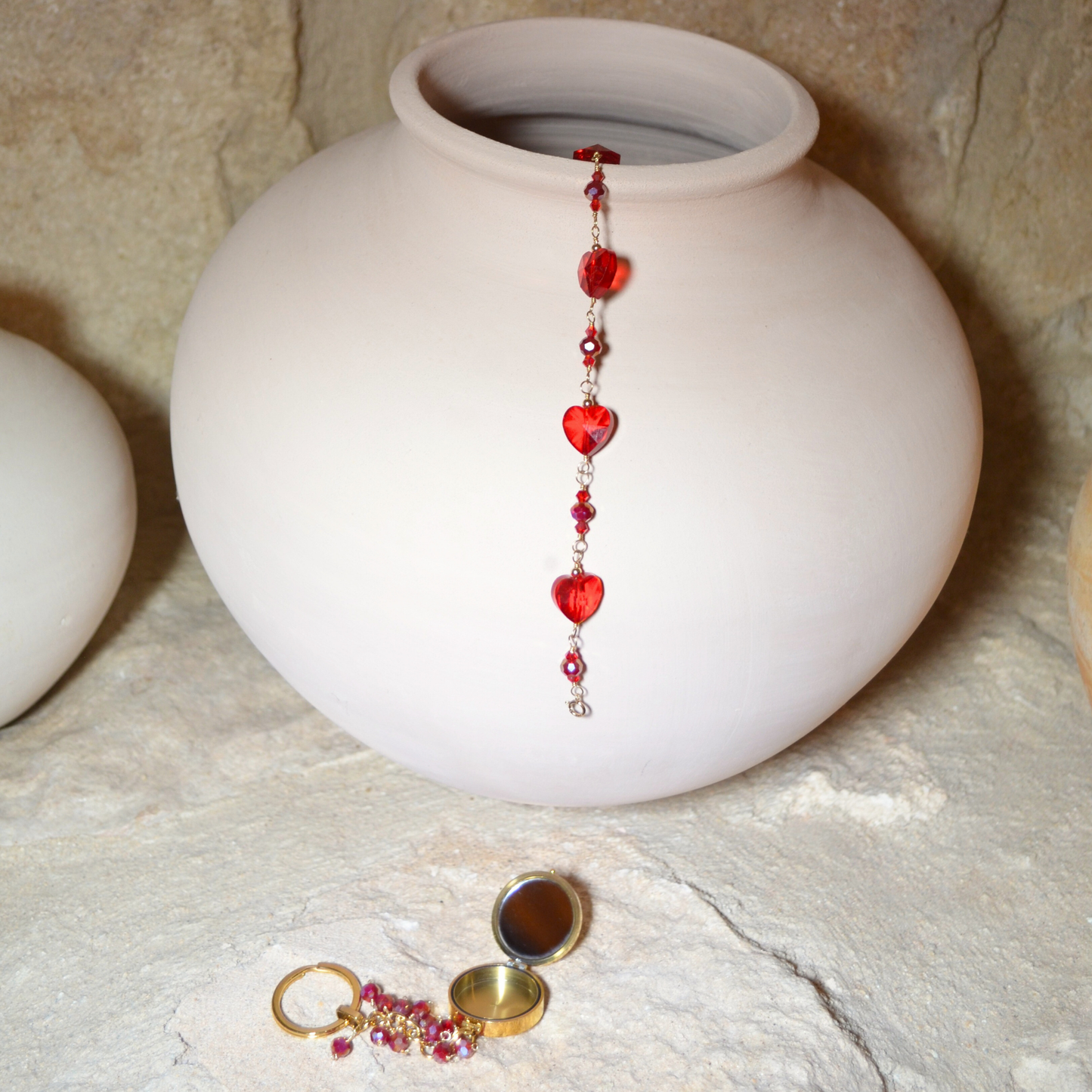 anuary Garnet-inspired bracelet with rich red crystals hanging elegantly in a vase, accompanied by the January Garnet Pocket Locket resting beneath it. Both pieces feature deep red hues symbolizing passion and protection, creating a stunning display of elegance and charm.