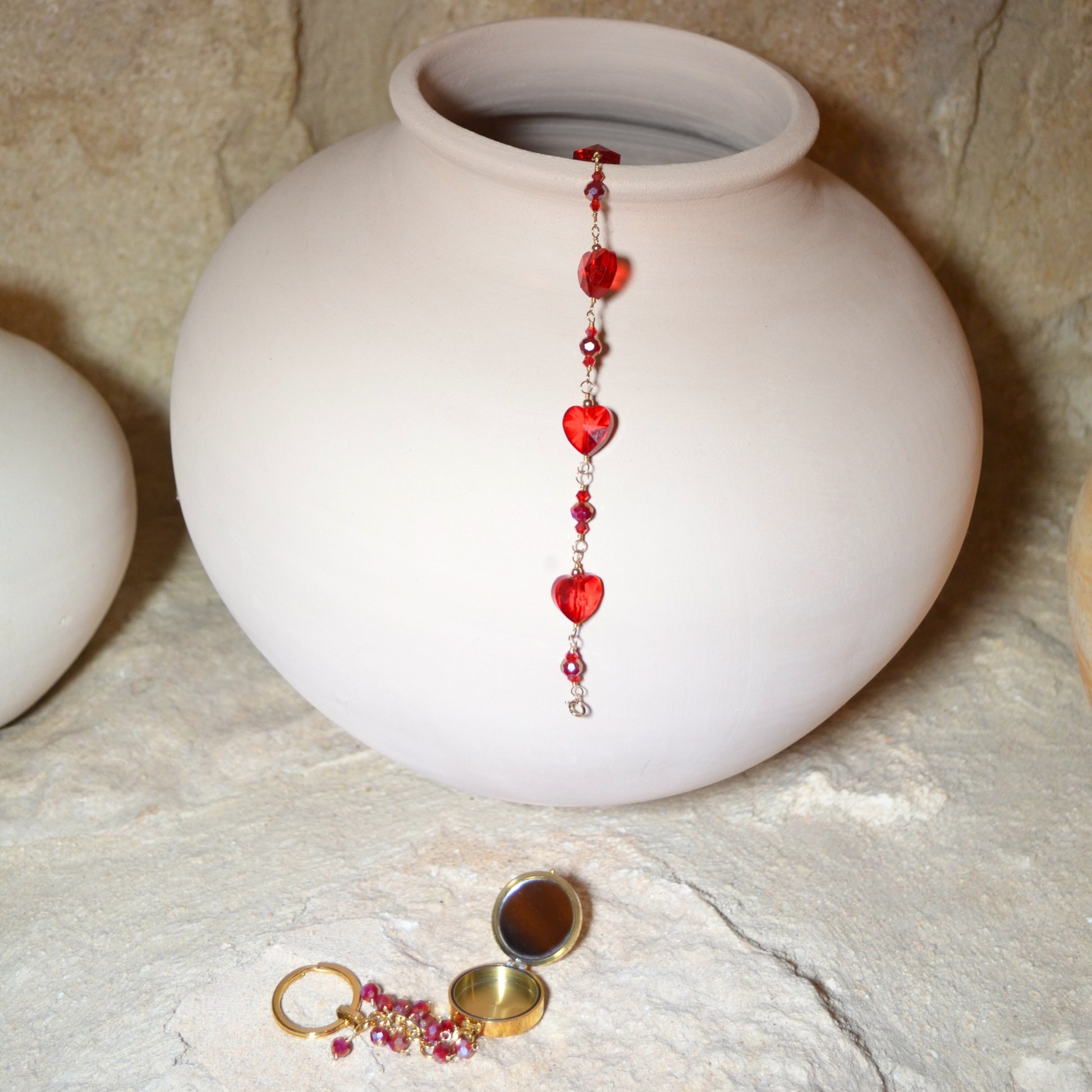 anuary Garnet-inspired bracelet with rich red crystals hanging elegantly in a vase, accompanied by the January Garnet Pocket Locket resting beneath it. Both pieces feature deep red hues symbolizing passion and protection, creating a stunning display of elegance and charm.