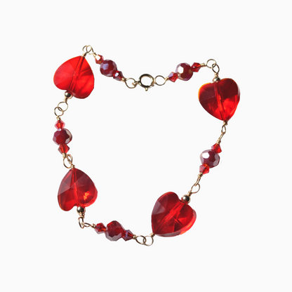A delicate red bracelet arranged in the shape of a heart, featuring sparkling glass crystals. The design highlights the elegance and romantic charm of the piece, making it a perfect symbol of love and connection.