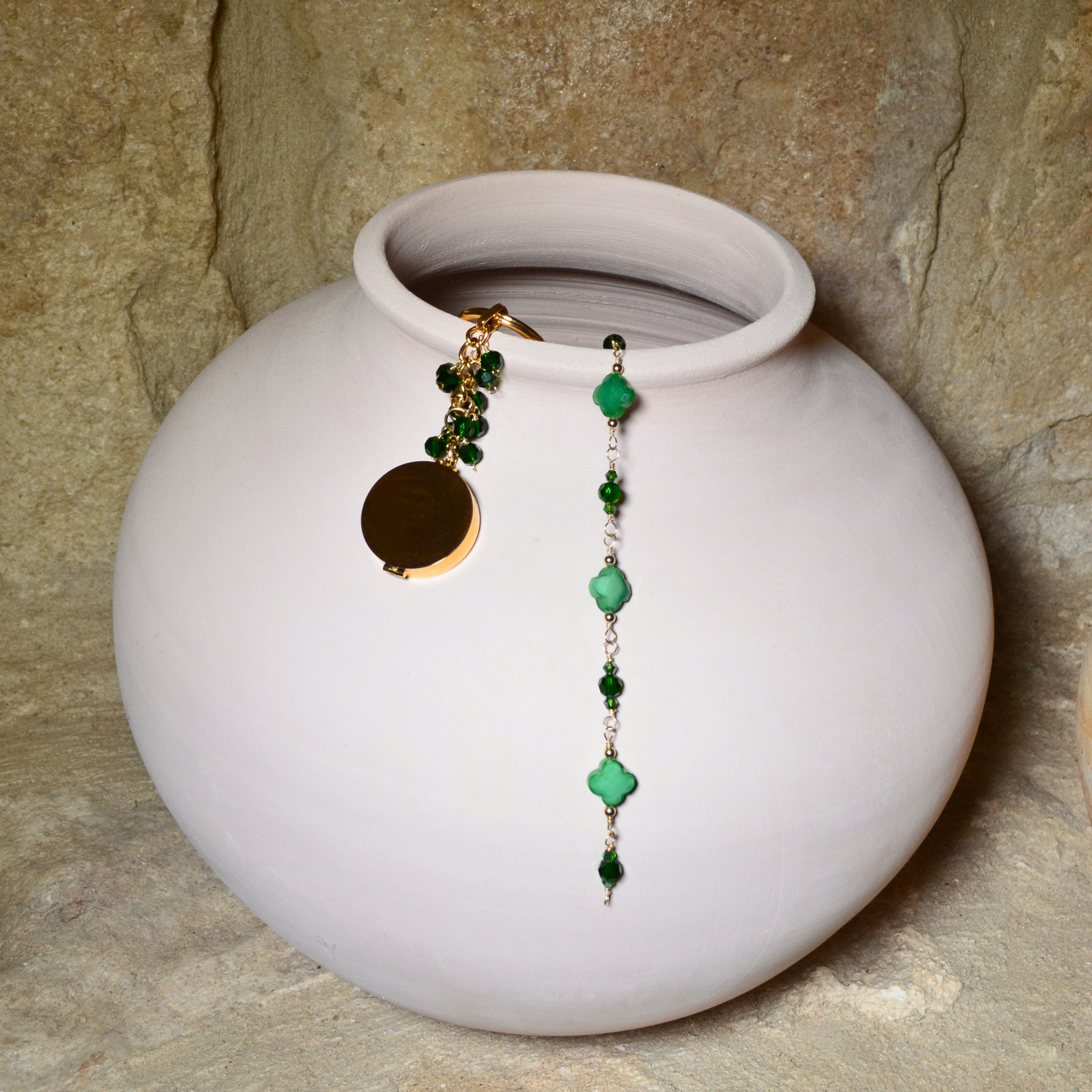 A beautiful May birthstone jewellery collection featuring an emerald inspired bracelet and pocket locket keychain, elegantly displayed on a white ceramic vase. Both pieces are handcrafted with 14k gold-filled wire and adorned with stunning emerald-inspired crystals.