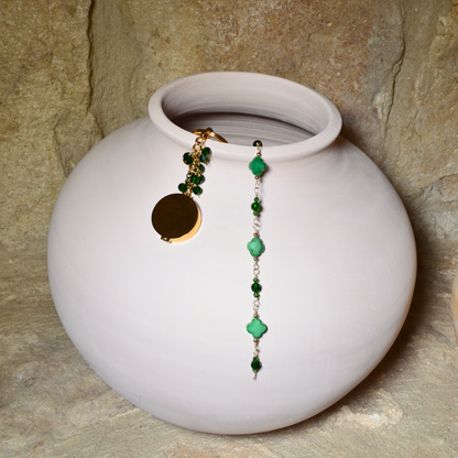 A beautiful May birthstone jewellery collection featuring an emerald inspired bracelet and pocket locket keychain, elegantly displayed on a white ceramic vase. Both pieces are handcrafted with 14k gold-filled wire and adorned with stunning emerald-inspired crystals.